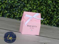 a pink box with a white ribbon on it sitting on a wooden table in front of some bushes