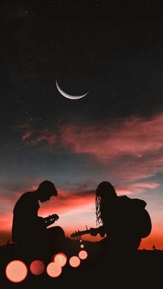 two people are sitting on the ground playing guitar at night with the moon in the background