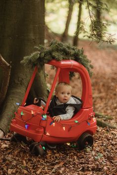 a baby sitting in a red toy car with christmas lights on it