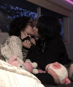 two women sitting on a bed kissing each other with stuffed animals in front of them