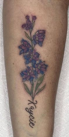 a tattoo on the leg of a woman with purple flowers and words written in cursive writing