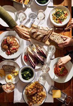 several people are sitting at a table with many plates and bowls of food on it