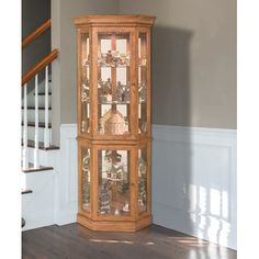 a tall wooden cabinet with glass doors in the middle of a room next to stairs