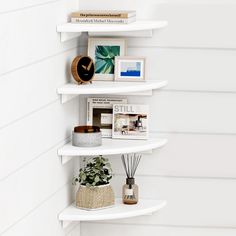 three white shelving shelves with pictures and plants on them in the corner of a room