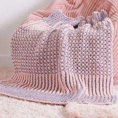 a crocheted blanket sitting on top of a white rug next to a pink chair