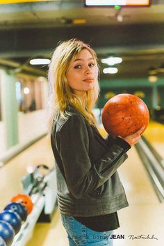 a woman holding an apple in her right hand while standing next to a bowling alley