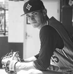 a black and white photo of a baseball player sitting in the dugout wearing a catchers mitt