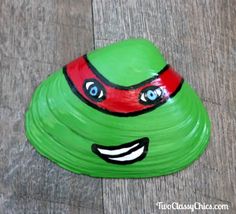 a green plastic toy with a red and black turtle on it's face, sitting on top of a wooden floor