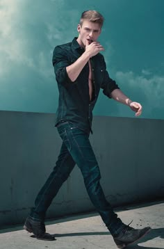 a man in black shirt and jeans walking on sidewalk with his hand under his chin