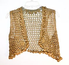 a crocheted top with gold beads hanging on a white hanger against a wall