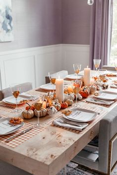 a dining room table with place settings and candles on the top, along with pumpkins