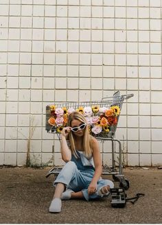 a woman sitting on the ground next to a shopping cart with sunflowers in it