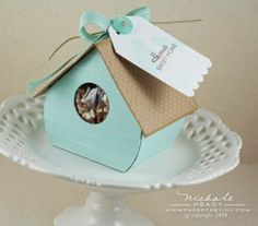 a small birdhouse with a tag attached to it's roof on a cake plate