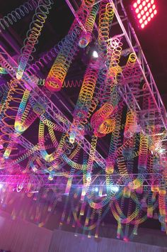 an art installation is lit up at night with colorful lights and spirals hanging from the ceiling