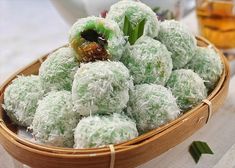 a basket filled with green and white desserts next to a cup of tea on a table