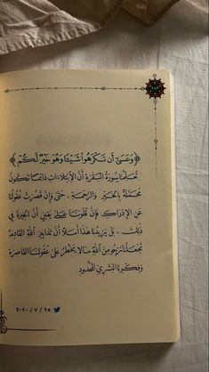 an open book with arabic writing on it sitting on top of a white table cloth