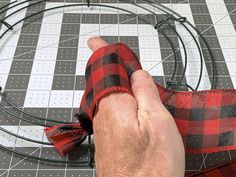 a person is tying a red and black plaid ribbon around a wire wreath on a table