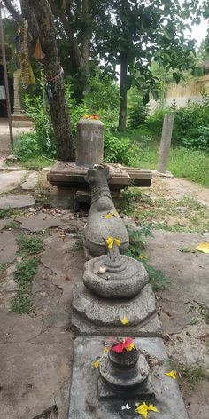 a stone statue with flowers on it in the middle of a park area next to a tree