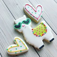 three decorated llama cookies sitting next to each other on a wooden table with hearts