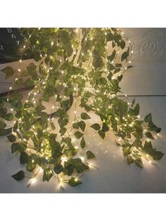 some lights that are on top of a white wall and green leaves hanging from the ceiling