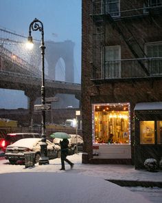 a person walking in the snow next to a street light with an overpass behind them