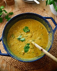 a blue pot filled with yellow soup and garnished with cilantro leaves