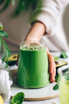 a person holding a green smoothie in front of a plate with leaves on it