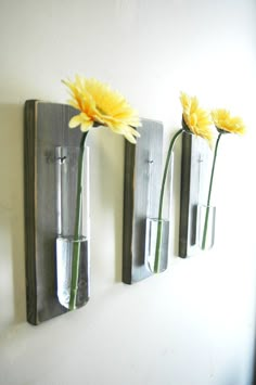 three metal vases with yellow flowers are hanging on the wall next to each other