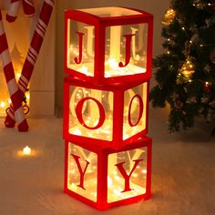 a lighted cube with the word joy spelled on it in front of a christmas tree