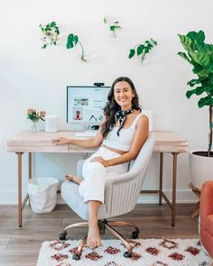 a woman sitting at a desk in front of a computer and potted plants on the wall