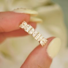 a woman's hand holding a diamond ring in her left hand, with white flowers in the background