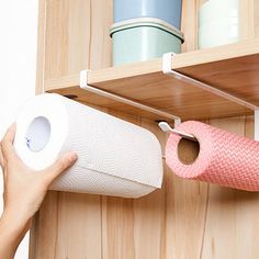 a person holding a roll of toilet paper in front of a wooden shelf with two rolls of toilet paper on it