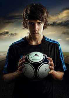 a young man holding a soccer ball in front of a dark sky with clouds behind him