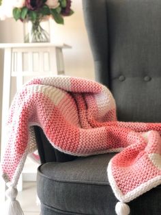 a pink and white blanket sitting on top of a chair next to a gray chair