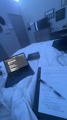 an open laptop computer sitting on top of a bed next to a sheet of paper