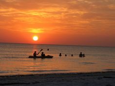 people are in the water at sunset on a beach