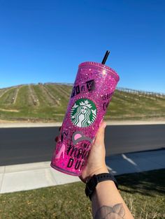 a person holding up a pink starbucks drink in front of a road and grassy area