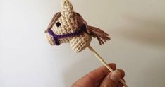 a hand holding a crocheted animal lollipop with a purple scarf on it