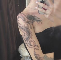 a woman with a dragon tattoo on her arm holding a cell phone in her hand