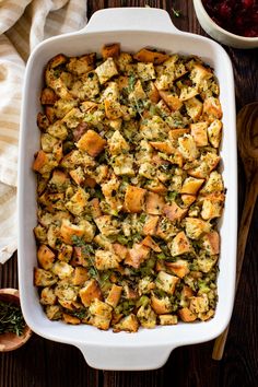 a casserole dish with stuffing in it on a wooden table next to a bowl of cranberry sauce