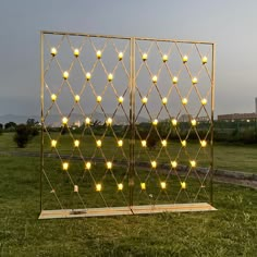 an outdoor sculpture in the middle of a grassy field with lights on it's sides