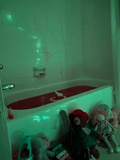 stuffed animals are sitting in the corner of a bathtub with green light on it