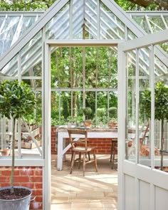 the inside of a greenhouse with glass walls and doors leading to an outside dining area