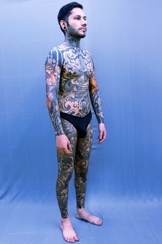 a man with tattoos on his body standing in front of a blue background