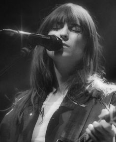 a woman singing into a microphone while holding a guitar