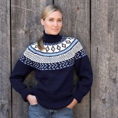 a woman standing in front of a wooden fence wearing a blue sweater with white and black designs on it