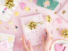 a woman's hands holding a gift box surrounded by wrapping paper and confetti