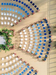 an aerial view of a beach with blue chairs and a wreath in the middle of it