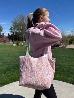 a woman carrying a pink flowered purse on her back while walking down a sidewalk