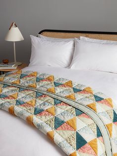 a bed with white pillows and quilted blanket on it's headboard, next to a lamp